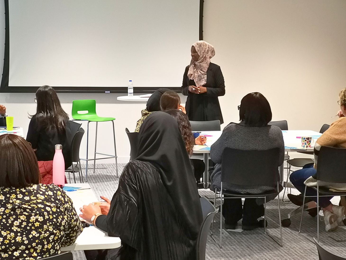 Olayinka Sanni standing at the front of a workshop room, facilitating a group of seated leaders